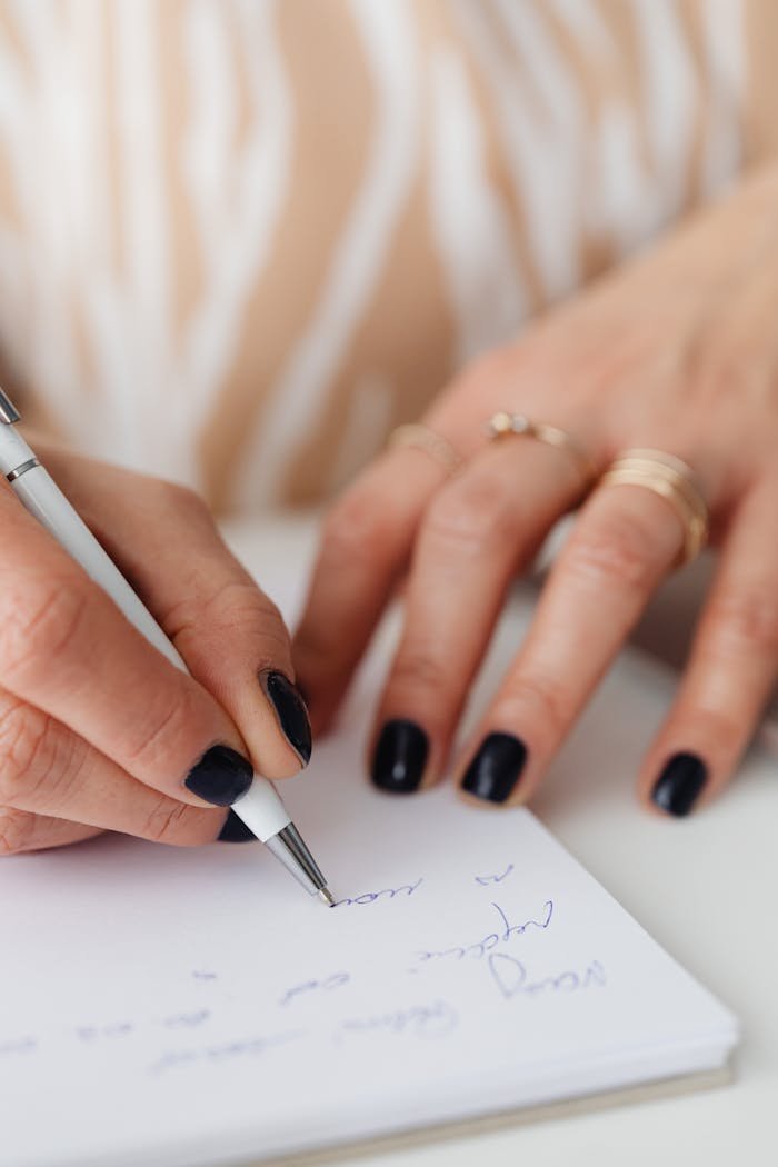 A close-up shot capturing a hand with manicured nails writing on paper in a notebook.